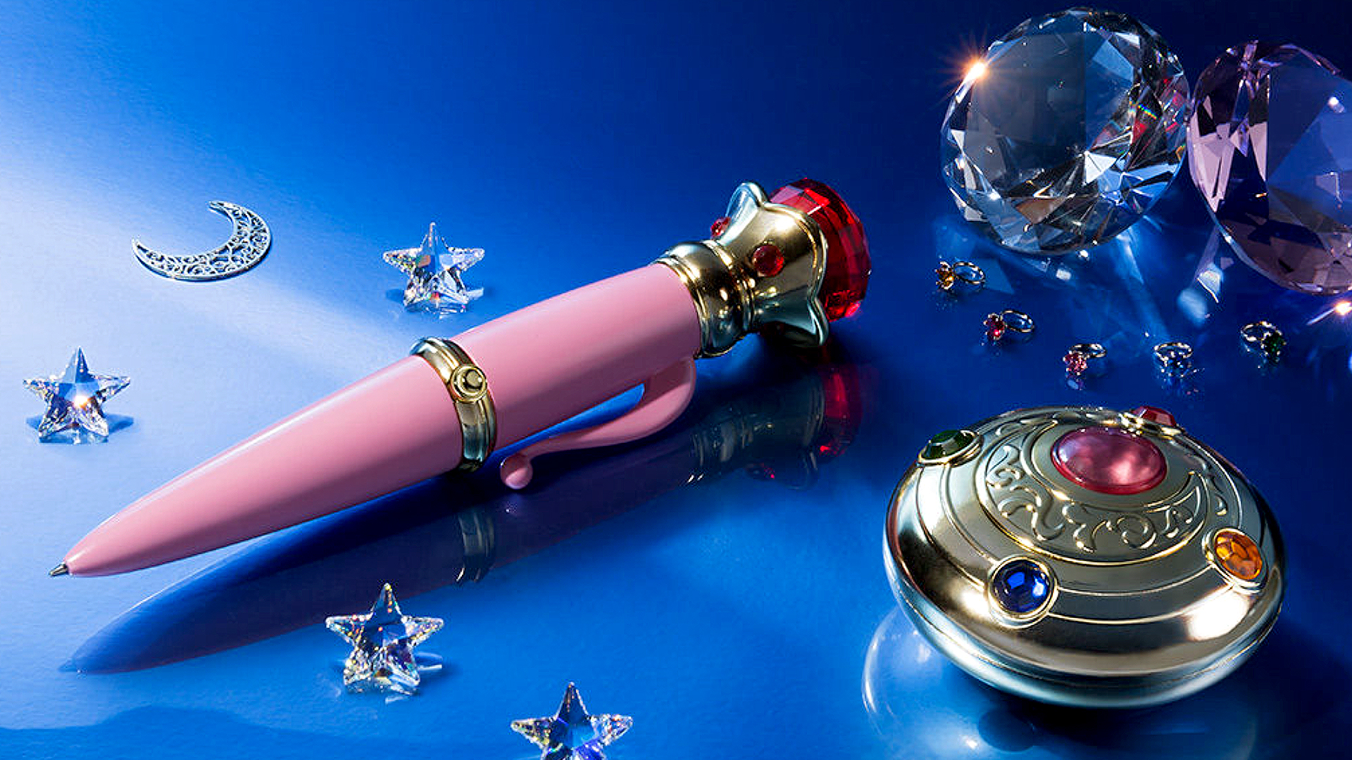 Sailor Moon Transformation Brooch & Disguise Pen Proplica Set next to diamond crystals on a blue background.