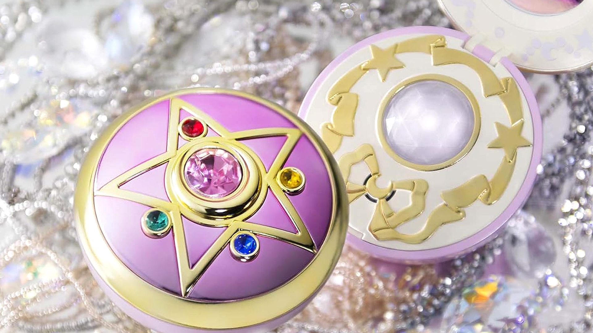 Two Sailor Moon Tamashii Nations Crystal Star Compact Proplica next to each other with one open and loads of crystals and jewelery behind them.